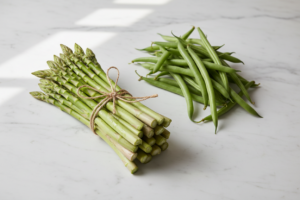 Asperges vertes fraîches et haricots verts crus côte à côte sur une surface blanche lumineuse.